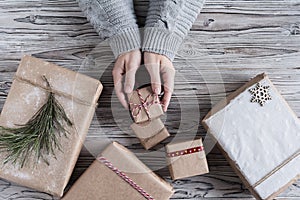 Female packing gifts. Cardboard box in craft paper, christmas rope and tree on the rustic wood planks background. DIY