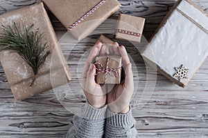 Female packing small gift. Cardboard box in craft paper, christmas rope and tree on the rustic wood planks background. DIY