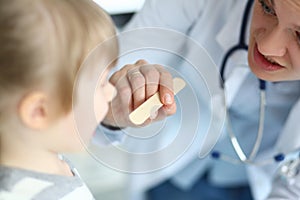 Female paediatrician examining little kid patient throat with wooden stick