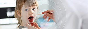 Female paediatrician examining little kid patient throat with wooden stick