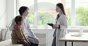 Female paediatrician talks to dad and little child during consultation