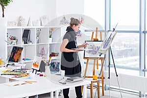 Female painter drawing in art studio using easel. Portrait of a young woman painting with aquarelle paints on white photo