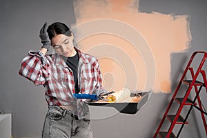 Female painter with headache holding painting roller while renovation her new house and painting walls
