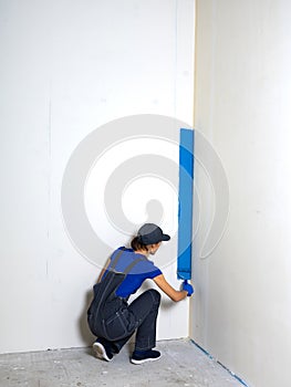 Female painter painting a white wall with a roller in blue color renovations or construction concept