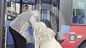 Female Passenger Helping Senior Woman To Board Bus