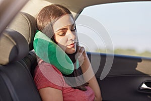 Female passenger sleeps in car while rides on long distance, uses small pillow as has pain in neck, takes nap, has rest, feels tir