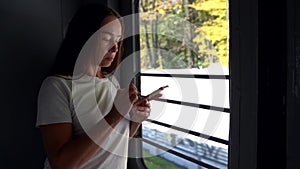 Female passenger of suburban train is using smartphone, standing in tambour, woman is travelling