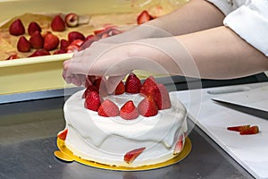 Female pastry chef hands, decorating a cream cake with strawberries.
