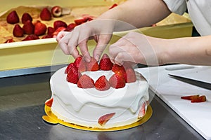 Female pastry chef hands, decorating a cream cake with strawberries.