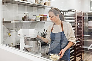 Female pastry chef using an electric mixer while preparing dough to cook in the kitchen.