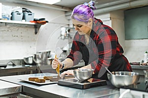 Female pastry chef wearing a apron decorating cake with a pastry bag with cream. Small baking business.