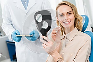 Female patient choosing tooth implant looking at mirror in modern