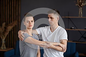 Female patient doing physical exercises with physiotherapist. Male therapist treating injured shoulder of young athlete