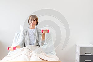 Female patient exercising with dumbbells in the hospital. Physiotherapist Assisting Senior Woman To Lift Dumbbells. the doctor is