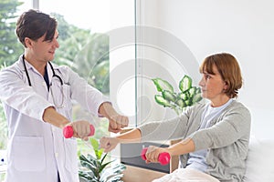 Female patient exercising with dumbbells in the hospital. Physiotherapist Assisting Senior Woman To Lift Dumbbells. the doctor is