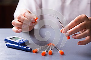 Female patient hands holding open insulin syringe, glucometer on the table