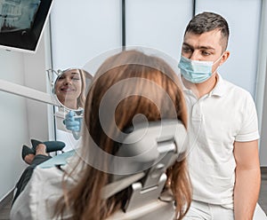 A female patient looks in a mirror showing her a dentist in a clinic. A woman in the clinic receives a full range of