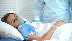 Female patient in oxygen mask sleeping, nurse standing by, surgery preparation