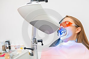 A female patient receives teeth whitening treatment, including the use of a UV lamp for bleaching.