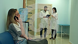 Female patient talking on the phone in hospital hall while two doctors consulting