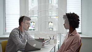 Female patient talking to male doctor and sitting at table in clinic office during visit spbd.