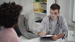 Female patient talking to male doctor and sitting at table during visit to clinic office spbd.