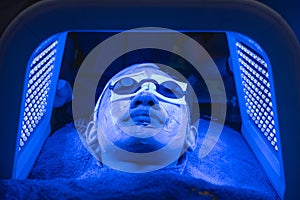 A female patient undergoes blue LED light therapy for skin rejuvenation at an aesthetic clinic. Using a phototherapy device