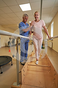 Female patient uses parallel bars to walk in rehab center