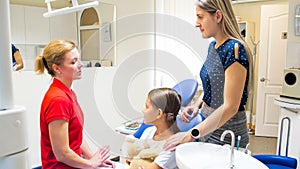 Female pediatric dentist talking to girl and her mother in dentist office