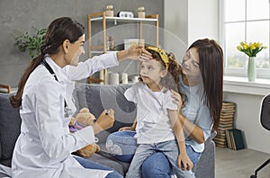 Female pediatrician checks the temperature of a little girl patient during a home visit.