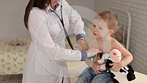 Female pediatrician examining cute little boy with stethoscope.
