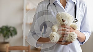 Female pediatrician holding teddy bear in hands, close up view