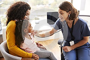 Female Pediatrician Wearing Scrubs Listening To Girls Chest With Stethoscope In Hospital Office