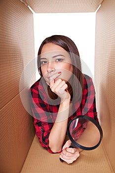 Female peeking into carton box looking through magnifying glass