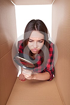 Female peeking into carton box looking through magnifying glass