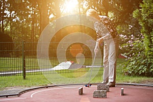 Female pensioner at a minigolf court hits a ball with an iron ra