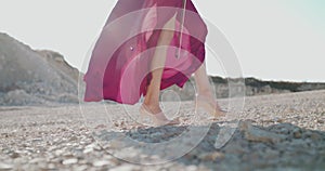 Female person in blowing dress and shoes with bow in hand walks on beach stones