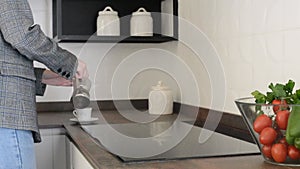 Female Person in Casual Clothes Pouring Coffee into a Cup in the Kitchen in Minimalist Style. Nutrition and lifestyle.