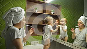 Female person and child brush teeth looking in large mirror