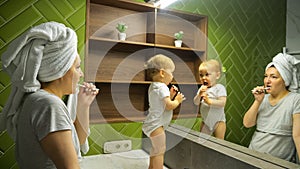 Female person and child brush teeth looking in large mirror