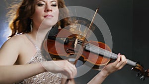 Female person emotionally plays on fiddle close up indoors philharmonic society on background of bright light and smoke