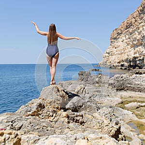 Female person in one-piece swimsuit walks on rocky seashore