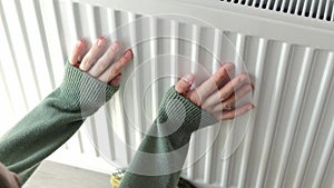 Female person puts feet in grey woolen socks on room central heating radiator. Owner gets cold and tries to warm up feet