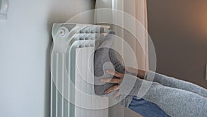 Female person putting feet in grey socks on heating radiator tries to warm up in cold apartment