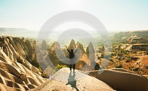 Female person stand with hands up over dramatic valley on hazy sunrise with fairy chimneys background. Solo exploration in Turkey