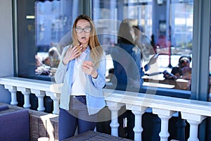 Female person standing at street cafe and using smartphone with fright emotion.