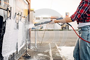 Female person with water gun cleans car mats