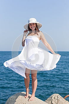 Female person in white hat and white sarong posing against sea