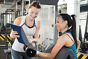 Female personal trainer helping young woman on her work out routines in gym.
