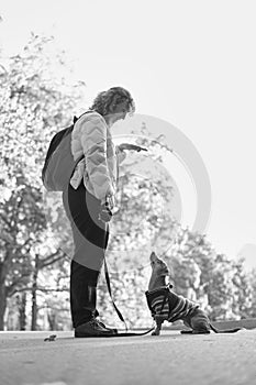 Female pet instructor in autumn clothes feeding dachshund puppy in autumn park